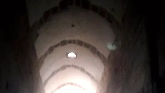 A vaulted corridor, the doorway at its far end the only light in it